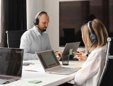 A man and a female wearing headsets working on laptops